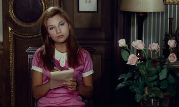Movie still from “Le Grand Amour” (1969), directed by Pierre Étaix – A woman in a pink dress writing on a piece of paper in front of pink roses; Medium shot, Over the shoulder angle