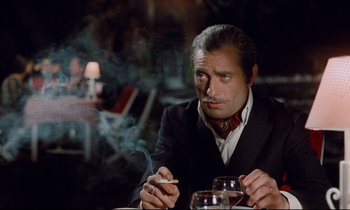Movie still from “Le Grand Amour” (1969), directed by Pierre Étaix – A man sitting at a table smoking a cigarette; Close Up shot, Over the shoulder angle