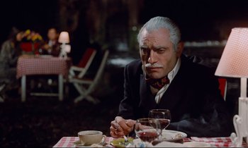 Movie still from “Le Grand Amour” (1969), directed by Pierre Étaix – An older man sitting at a dinner table smoking a cigarette; Medium shot, Over the shoulder angle