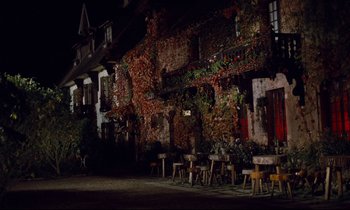 Movie still from “Le Grand Amour” (1969), directed by Pierre Étaix – An outdoor restaurant with tables and chairs outside of a building at night; Extreme Wide shot, High angle