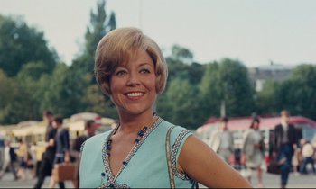 Movie still from “Le Grand Amour” (1969), directed by Pierre Étaix – A woman in a blue dress smiling for the camera; Close Up shot, Low angle