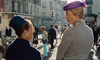 Movie still from “Le Grand Amour” (1969), directed by Pierre Étaix – Two older women talking on the sidewalk of a busy street; Medium shot, Over the shoulder angle