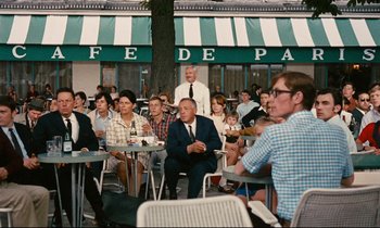 Movie still from “Le Grand Amour” (1969), directed by Pierre Étaix – A group of people sitting at tables in front of a restaurant; Wide shot, Over the shoulder angle