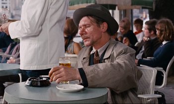 Movie still from “Le Grand Amour” (1969), directed by Pierre Étaix – A man sitting at a table holding a glass of beer; Medium shot, Over the shoulder angle