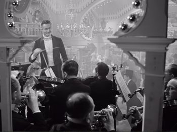 Movie still from “Le Plaisir” (1952), directed by Max Ophüls – A group of people in a room with a man holding a guitar; Wide shot, Low angle