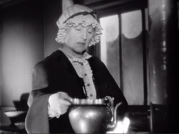 Movie still from “Le Plaisir” (1952), directed by Max Ophüls – An older woman in a hat is stirring a pot; Medium shot, Low angle