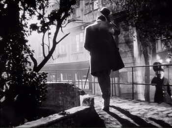 Movie still from “Le Plaisir” (1952), directed by Max Ophüls – A black and white photo of a man walking on the sidewalk; Wide shot, Low angle