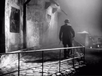 Movie still from “Le Plaisir” (1952), directed by Max Ophüls – A man in a hat and coat walking down a street; Wide shot, High angle