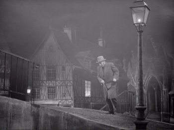 Movie still from “Le Plaisir” (1952), directed by Max Ophüls – A man in a hat and coat walking down a street; Extreme Wide shot, High angle