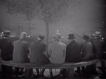 Movie still from “Le Plaisir” (1952), directed by Max Ophüls – A black and white photo of a group of men sitting on a bench; Wide shot, High angle