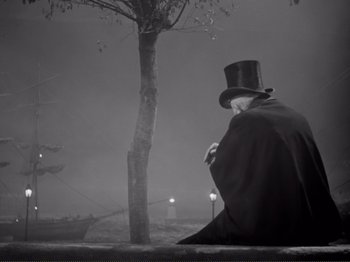 Movie still from “Le Plaisir” (1952), directed by Max Ophüls – A man in a top hat and a cape sitting in front of a tree in the fog; Wide shot, Low angle