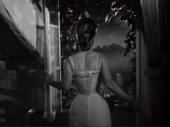 Movie still from “Le Plaisir” (1952), directed by Max Ophüls – A black and white photo of a woman in a corset looking out of a window; Medium shot, Low angle