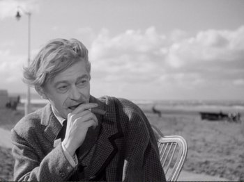 Movie still from “Le Plaisir” (1952), directed by Max Ophüls – A black and white photo of a man sitting on a chair; Medium shot, Low angle