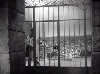 Movie still from “Le Plaisir” (1952), directed by Max Ophüls – A man standing in front of an iron gate; Wide shot, Low angle