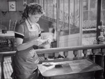 Movie still from “Le Plaisir” (1952), directed by Max Ophüls – An old photo of a woman in an apron looking at a piece of paper; Medium shot, Low angle