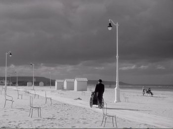 Movie still from “Le Plaisir” (1952), directed by Max Ophüls – A person riding a bike on a beach next to chairs; Extreme Wide shot, High angle