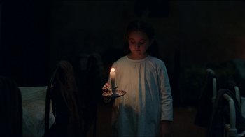A little girl is holding a lit candle in the dark