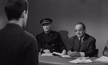 Movie still from “The Hole” (1960), directed by Jacques Becker – Two men in uniform sitting in front of a man; Medium shot, Over the shoulder angle