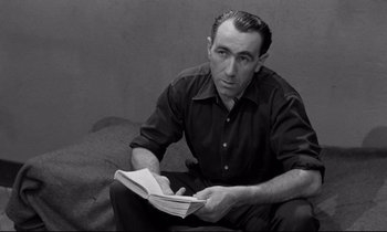 Movie still from “The Hole” (1960), directed by Jacques Becker – A black and white photo of a man reading a book; Medium shot, High angle