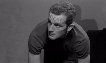 Movie still from “The Hole” (1960), directed by Jacques Becker – Black and white photograph of a man looking at the camera; Close Up shot, Low angle