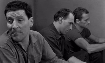 Movie still from “The Hole” (1960), directed by Jacques Becker – A group of men sitting next to each other in front of a wall; Medium shot, High angle