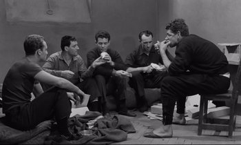 Movie still from “The Hole” (1960), directed by Jacques Becker – A group of men sitting on the ground eating; Medium shot, High angle