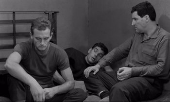 Movie still from “The Hole” (1960), directed by Jacques Becker – A group of men sitting next to each other on the ground; Medium shot, High angle
