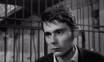 Movie still from “The Hole” (1960), directed by Jacques Becker – A man in a suit and tie in front of a jail cell; Close Up shot, Low angle