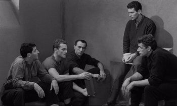 Movie still from “The Hole” (1960), directed by Jacques Becker – A black and white photo of a group of men sitting around; Medium shot, High angle