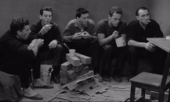 Movie still from “The Hole” (1960), directed by Jacques Becker – A group of men sitting next to each other eating food; Medium shot, High angle