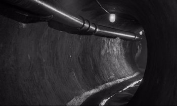 Movie still from “The Hole” (1960), directed by Jacques Becker – A black - and - white photo of a tunnel with water coming out of it; Wide shot, High angle