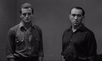 Movie still from “The Hole” (1960), directed by Jacques Becker – A black and white photo of two men standing next to each other; Medium shot, Low angle