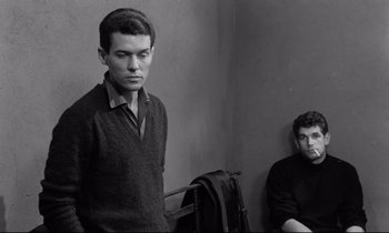 Movie still from “The Hole” (1960), directed by Jacques Becker – A man standing next to another man sitting on a wall; Medium shot, Over the shoulder angle