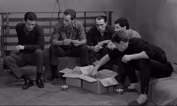Movie still from “The Hole” (1960), directed by Jacques Becker – A black and white photo of a group of men sitting around a box; Medium shot, High angle