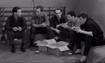 Movie still from “The Hole” (1960), directed by Jacques Becker – A group of men sitting on a bench next to a box; Medium shot, High angle