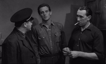 Movie still from “The Hole” (1960), directed by Jacques Becker – A group of men standing next to each other in a room; Medium shot, Over the shoulder angle