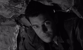 Movie still from “The Hole” (1960), directed by Jacques Becker – A black and white photo of a man looking at the camera; Close Up shot, Low angle