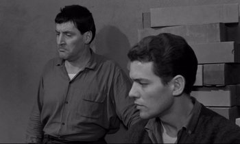 Movie still from “The Hole” (1960), directed by Jacques Becker – Two men sitting next to each other in front of a wall; Medium shot, High angle