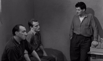 Movie still from “The Hole” (1960), directed by Jacques Becker – A group of men sitting next to each other in front of a wall; Medium shot, High angle
