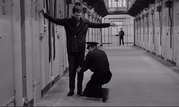Movie still from “The Hole” (1960), directed by Jacques Becker – A man kneeling down next to another man in a jail cell; Wide shot, Low angle