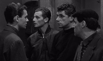 Movie still from “The Hole” (1960), directed by Jacques Becker – A group of men standing next to each other in a room; Medium shot, Over the shoulder angle