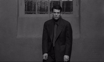 Movie still from “The Hole” (1960), directed by Jacques Becker – A man wearing a suit and tie standing in front of a building; Medium shot, Low angle