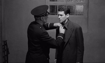 Movie still from “The Hole” (1960), directed by Jacques Becker – An officer adjusting the collar of a young man; Medium shot, Low angle