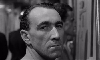 Movie still from “The Hole” (1960), directed by Jacques Becker – Black and white photograph of a man looking at the camera; Close Up shot, Low angle