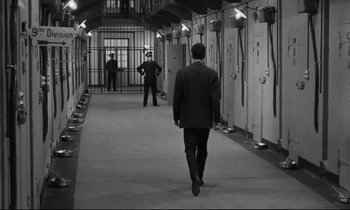 Movie still from “The Hole” (1960), directed by Jacques Becker – A man in a suit walking down a hallway; Wide shot, High angle