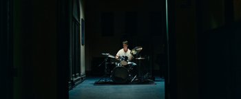 Movie still from “Whiplash” (2014), directed by Damien Chazelle – A young man playing drums in a dark room; Wide shot, High angle