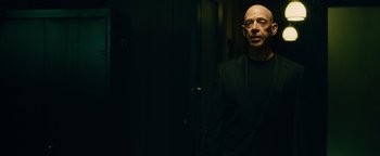 Movie still from “Whiplash” (2014), directed by Damien Chazelle – A bald man in a black suit standing in a dark room; Medium shot, Low angle