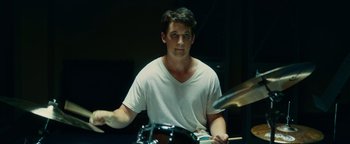 Movie still from “Whiplash” (2014), directed by Damien Chazelle – A man playing a drum set in a dark room; Close Up shot, Low angle