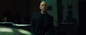 Movie still from “Whiplash” (2014), directed by Damien Chazelle – A bald man in a black suit is sitting in a room; Medium shot, Low angle