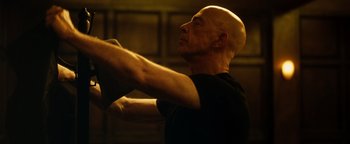 Movie still from “Whiplash” (2014), directed by Damien Chazelle – A bald man with a shaved head is stretching; Close Up shot, Low angle
